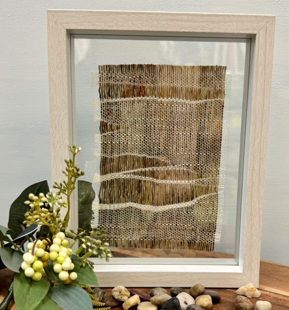 Explore "Whispering Meadows" by Ashculme Textiles, an intricate artwork made from hand-reared alpaca wool and silk, dyed with natural bush leaves. This piece captures the serene beauty of the Australian outback, framed between glass panels for a detailed and captivating display.